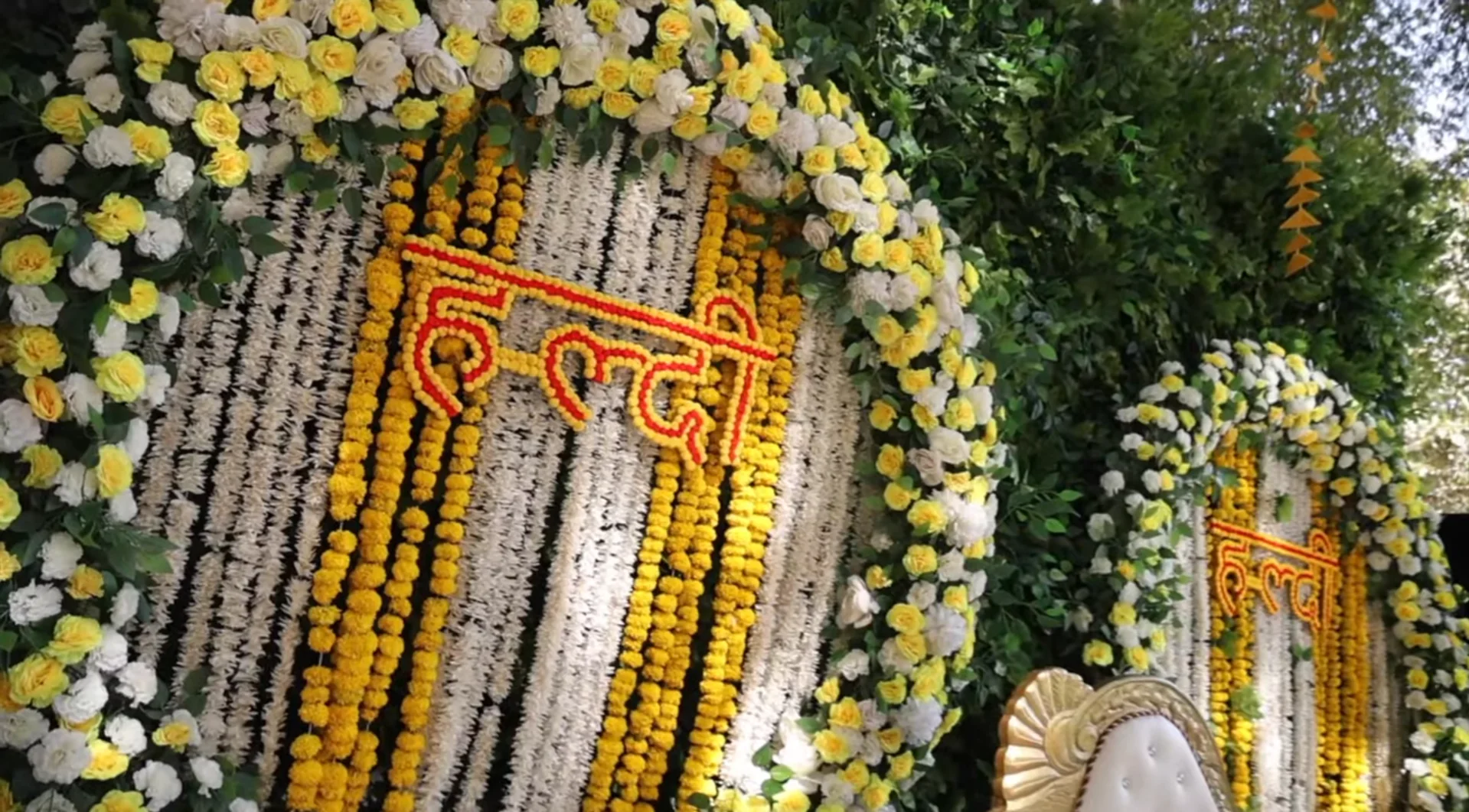 Haldi floral backdrop with हल्दी lettering made from marigolds over strings of marigold and white flowers, framed by yellow and white roses